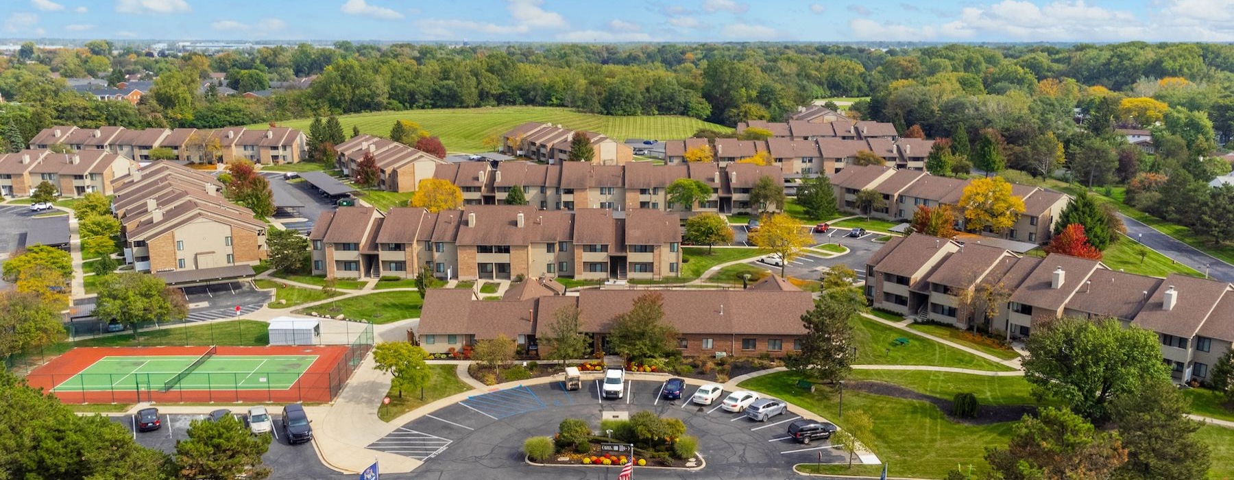 aerial view of a community surrounded by trees with a tennis court and parking lot